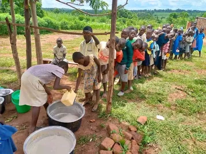 Children lined up outdoors for a meal near a pile of construction bricks
