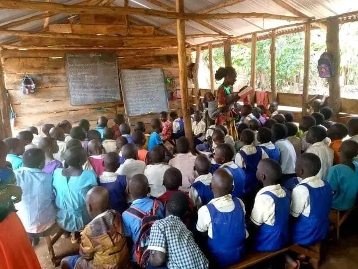 Teacher with a baby on her back leading a packed classroom